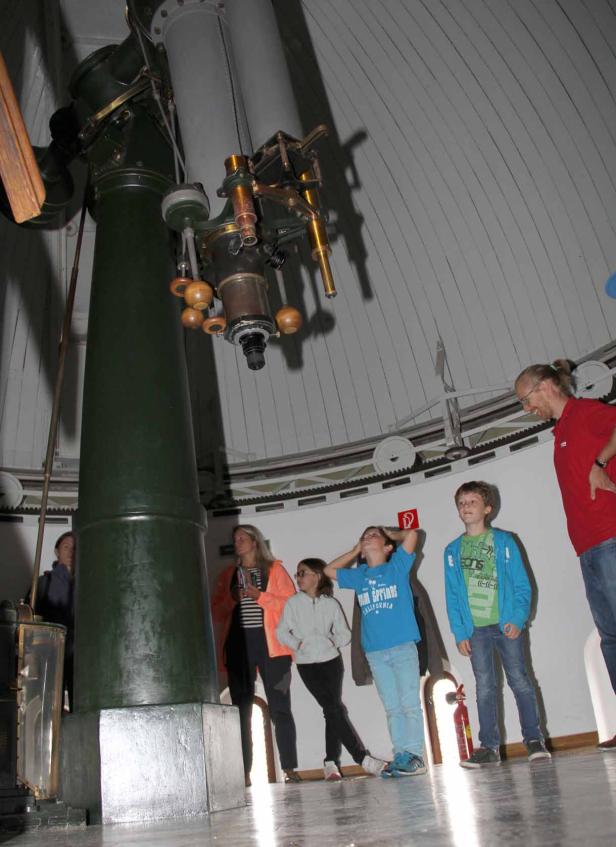 Eine Gruppe von Menschen steht in einem Observatorium unter einem großen Teleskop.
