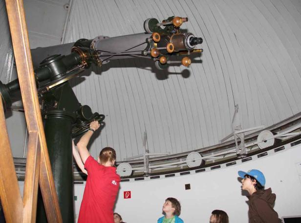 Eine Gruppe von Kindern beobachtet ein großes Teleskop in einer Sternwarte.