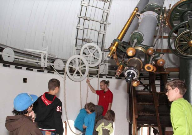 Eine Gruppe von Kindern steht unter einem großen Teleskop in einer Sternwarte.