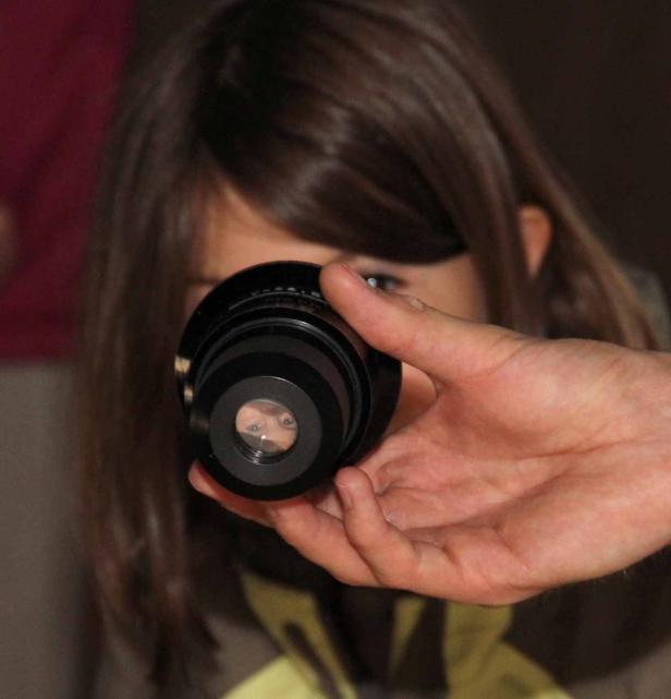 Ein Mädchen blickt durch ein Objektiv, das von einer Hand gehalten wird.
