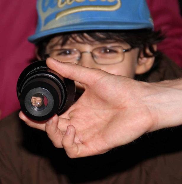 Ein Junge mit Brille hält ein Objektiv vor sein Gesicht.