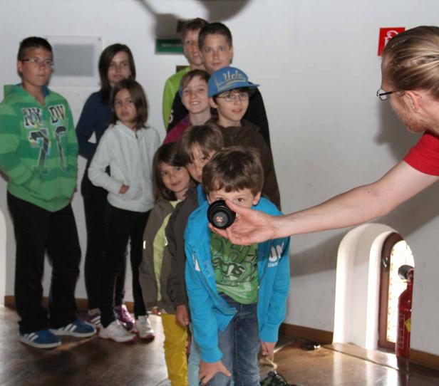 Eine Gruppe Kinder steht in einer Reihe, während ein Mann mit einer Kameralinse hantiert.