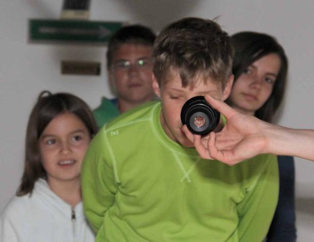 Ein Junge blickt durch ein Kameraobjektiv, umgeben von anderen Kindern.