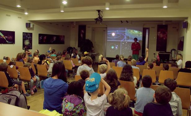 Ein Mann hält einen Vortrag über das Sonnensystem vor einer Gruppe von Kindern.