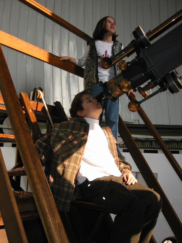 Zwei Kinder benutzen ein großes Teleskop in einem Observatorium.