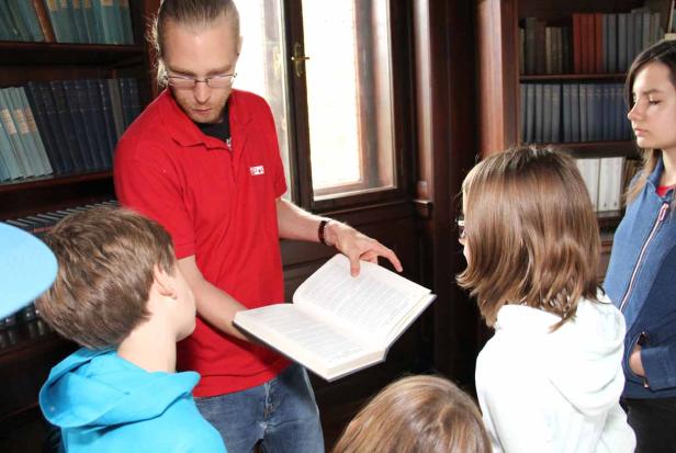 Ein Mann liest einer Gruppe von Kindern in einer Bibliothek aus einem Buch vor.