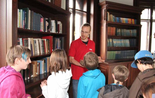 Eine Gruppe Kinder hört einem Mann in einer Bibliothek zu.