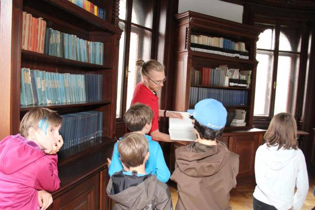 Eine Gruppe von Kindern hört einem Mann in einer Bibliothek zu.