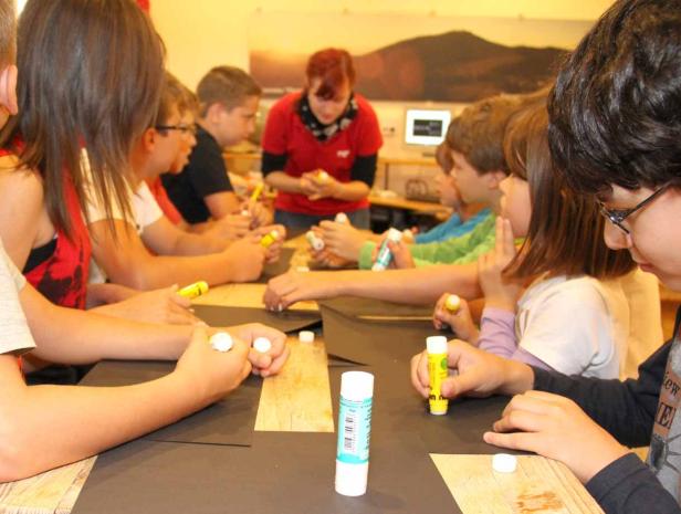 Eine Gruppe Kinder bastelt mit Klebstoff und Papier an einem Tisch.