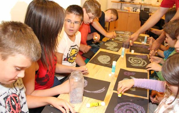 Eine Gruppe Kinder bastelt mit Kleber und Glitzer auf schwarzem Papier.