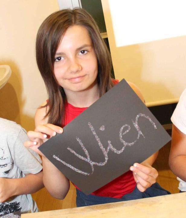 Ein junges Mädchen hält ein schwarzes Blatt Papier mit dem glitzernden Wort „Wien“ darauf.