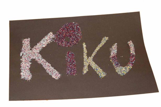 Das Wort „Kiku“ ist mit Glitzer auf ein schwarzes Blatt Papier geschrieben.