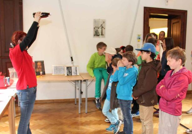 Eine Frau demonstriert vor einer Gruppe von Kindern ein Experiment mit einer Flasche.
