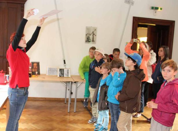 Eine Frau erklärt einer Gruppe von Kindern etwas anhand von Papierblättern.