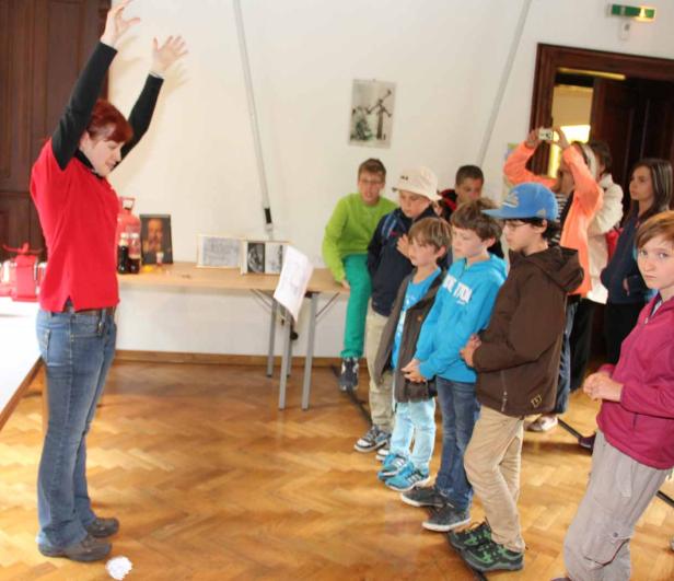 Eine Frau erklärt einer Gruppe von Kindern etwas in einem Raum.