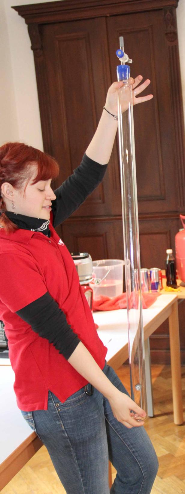 Eine Frau mit roten Haaren hält ein langes, durchsichtiges Rohr in der Hand.