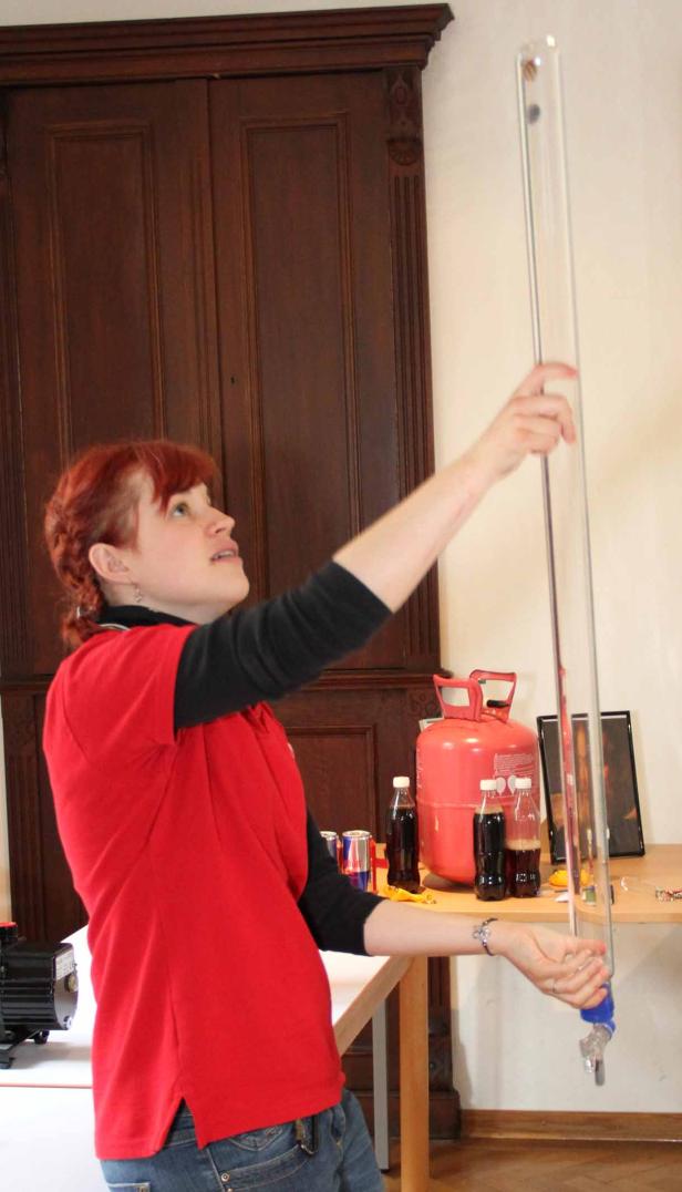 Eine Frau mit roten Haaren experimentiert mit einer langen Röhre und Flüssigkeiten.