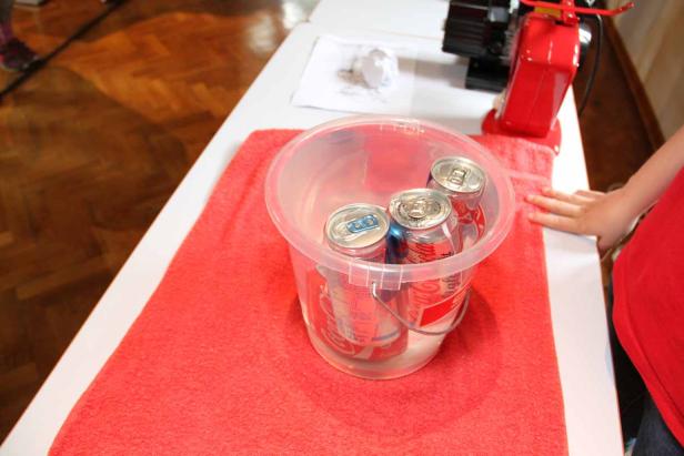 Ein durchsichtiger Eimer mit mehreren Dosen Coca-Cola auf einem roten Tuch.