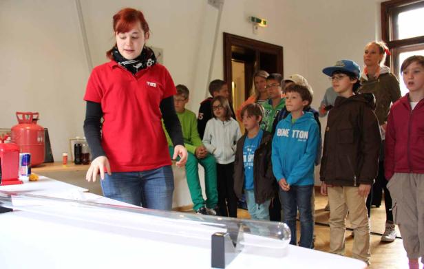 Eine Frau erklärt einer Gruppe von Kindern ein Experiment mit einer Röhre.