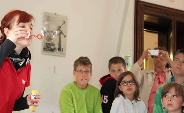 Eine Frau macht Seifenblasen vor einer Gruppe von Kindern.