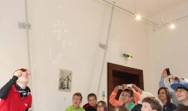 Eine Frau macht Seifenblasen, während eine Gruppe Kinder sie beobachtet und fotografiert.