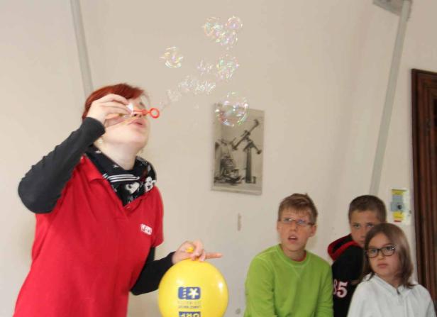 Eine Frau macht Seifenblasen, während Kinder zuschauen.