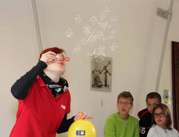 Eine Frau pustet Seifenblasen, während Kinder zuschauen.