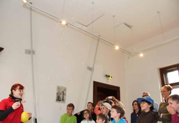 Eine Frau macht Seifenblasen für eine Gruppe von Kindern in einem Raum.