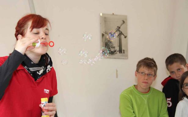 Eine Frau pustet Seifenblasen, während Kinder zusehen.