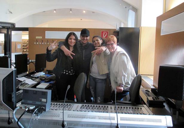 Vier Personen posieren vor einem Mischpult in einem Aufnahmestudio.