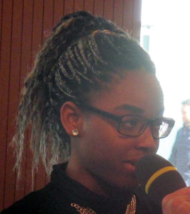 Eine Frau mit Brille und Zöpfen spricht in ein Mikrofon.