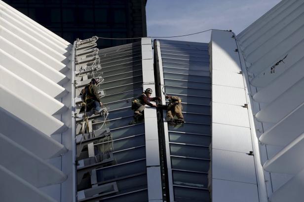 Drei Fensterputzer arbeiten an der Fassade eines hohen Gebäudes.