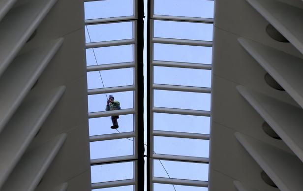 Ein Fensterputzer hängt an Seilen und reinigt eine hohe Glasdecke.