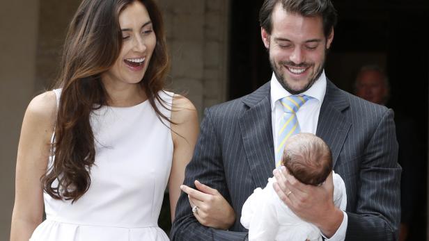 Ein Mann im Anzug hält ein Baby, während eine Frau lächelt.