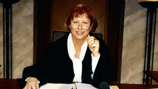 Eine Frau mit Brille und Richterrobe sitzt an einem Schreibtisch.