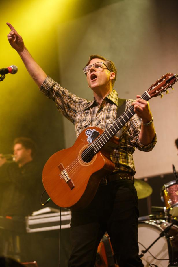 Ein Mann mit Brille spielt Gitarre und singt auf einer Bühne.