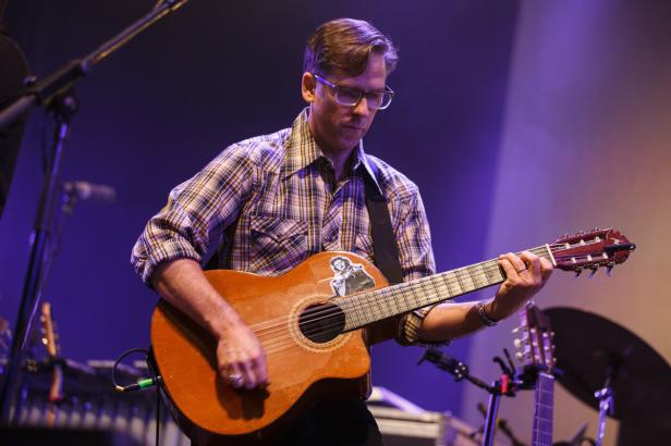 Ein Mann mit Brille spielt Gitarre auf einer Bühne.