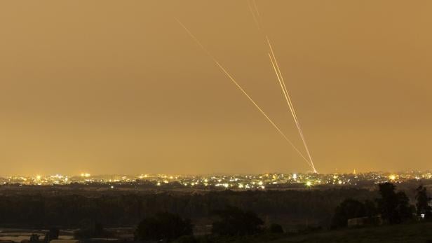 Drei Raketen steigen über einer beleuchteten Stadt in den orangefarbenen Nachthimmel auf.