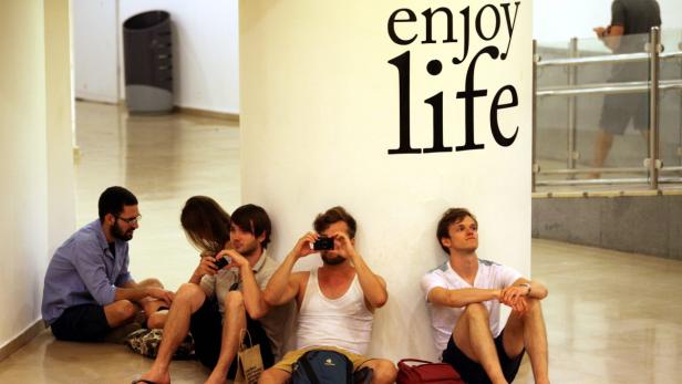 Eine Gruppe junger Leute sitzt an einer Wand mit der Aufschrift „enjoy life“.