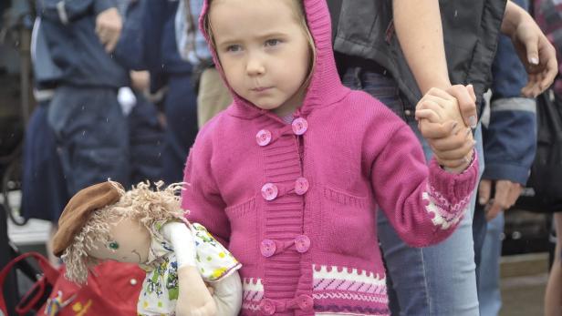 Ein kleines Mädchen hält die Hand eines Erwachsenen und eine Stoffpuppe.