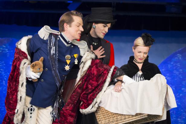 Drei Schauspieler in Kostümen betrachten ein Baby in einem Korb.