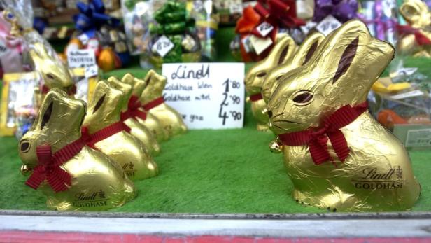 Mehrere goldene Lindt-Schokoladenhasen mit roten Schleifen stehen auf einem Tisch zum Verkauf.