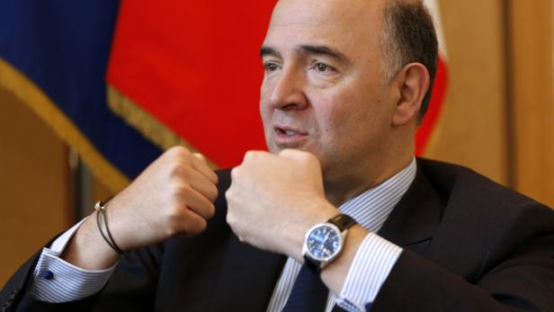 Ein Mann in Anzug gestikuliert vor einer blau-roten Flagge.