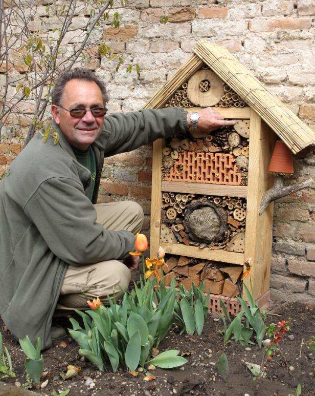 Ein Mann kniet neben einem Insektenhotel im Garten.