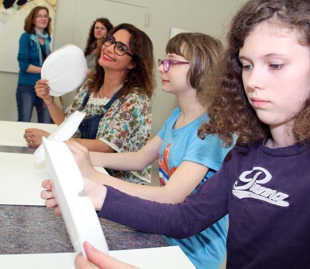 Eine Frau und zwei Mädchen basteln mit weißen Styropor-Formen an einem Tisch.