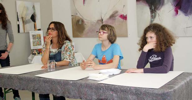 Drei Personen sitzen an einem Tisch mit Papier und blicken aufmerksam in verschiedene Richtungen.