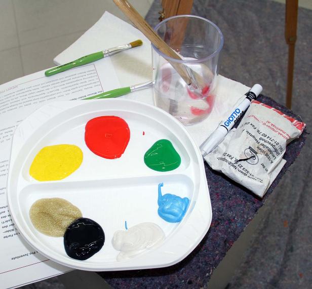 Eine Farbpalette mit verschiedenen Farben, Pinseln und einem Wasserglas.