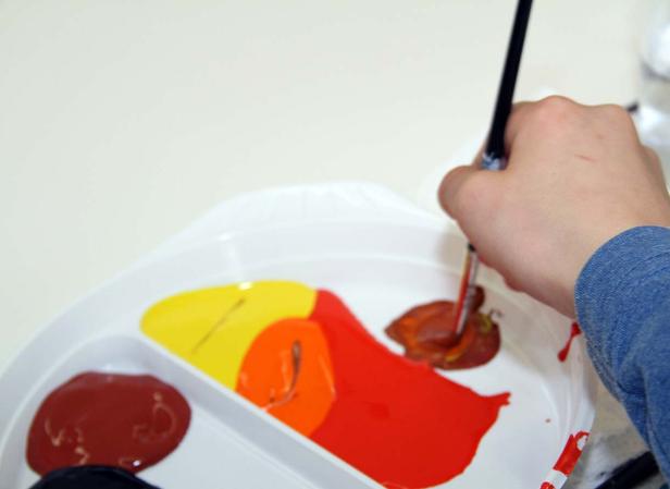 Eine Hand mischt mit einem Pinsel Farben auf einer Palette.