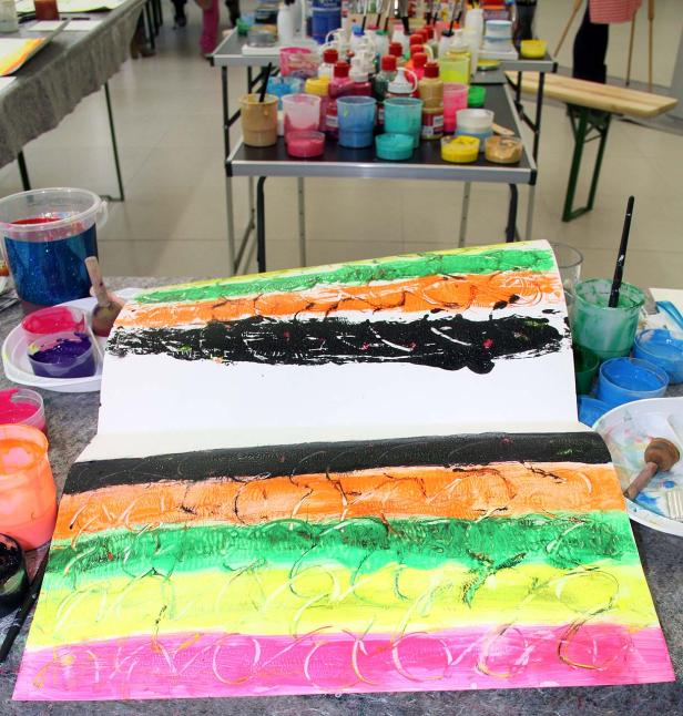 Ein abstraktes Gemälde mit horizontalen Streifen in verschiedenen Farben liegt auf einem Tisch.