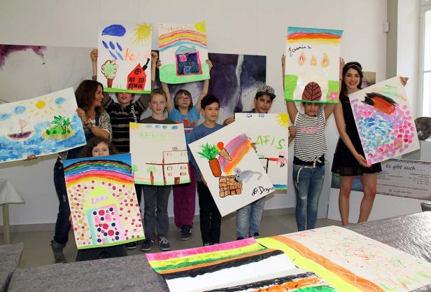 Eine Gruppe von Kindern und zwei Frauen präsentieren stolz ihre bunten Gemälde.